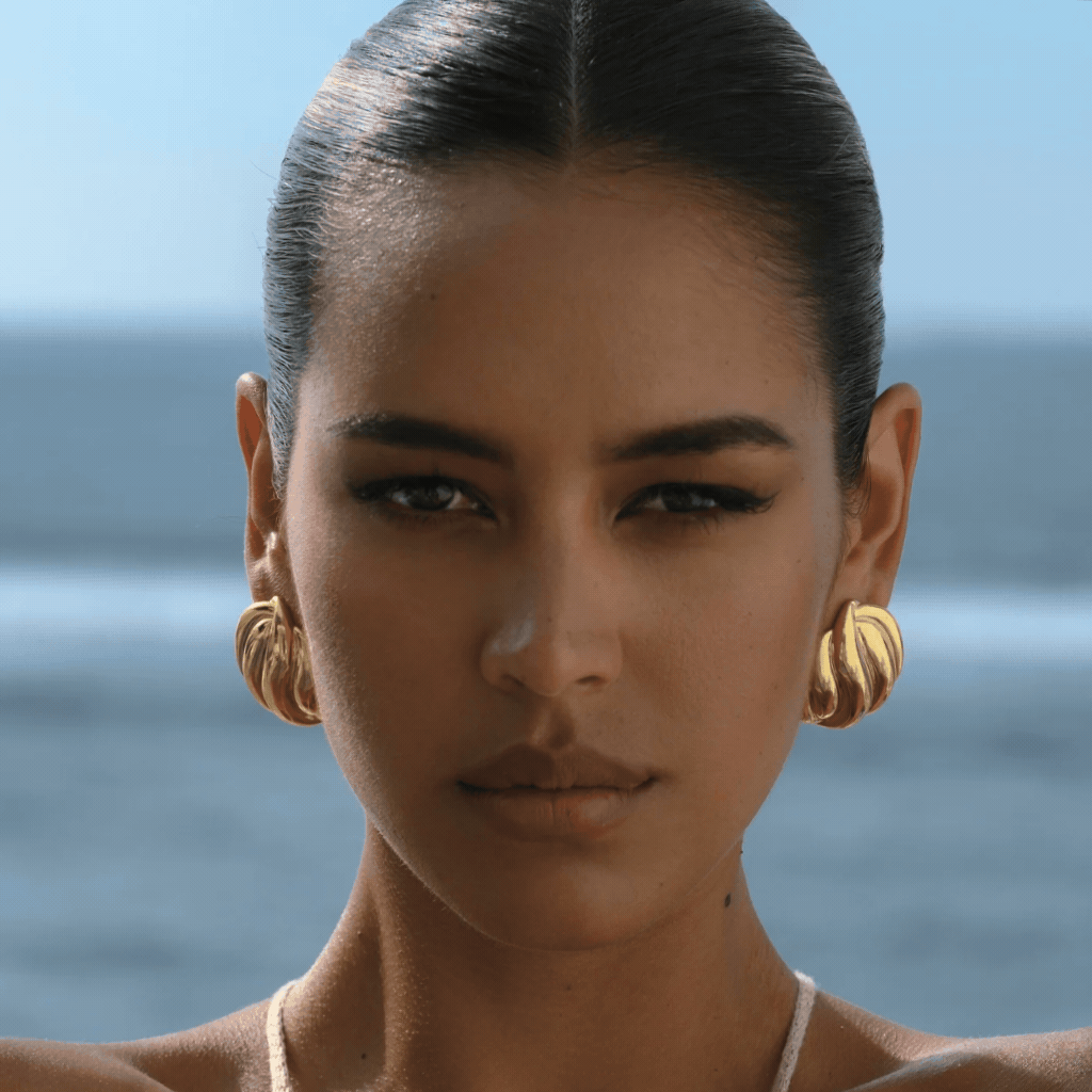 gold statement earrings at the back drop of the ocean
