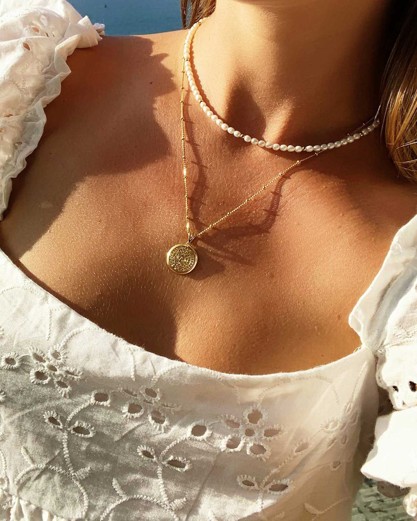 neck of girl wearing one pearl and one gold and coin necklace