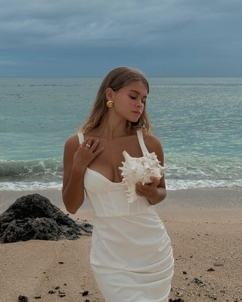 gold shell earrings at the bride in white dress holding a shell at the beach