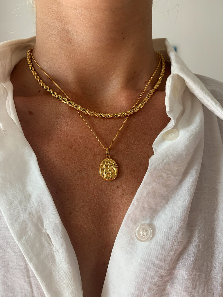 a women wearing white shirt and layered gold necklace, twisted chain necklace and oval pendant necklace