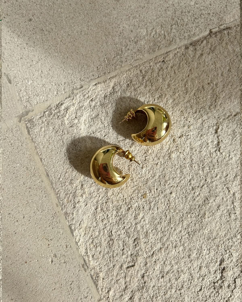 chunky gold earrings flatlay on a stone surface