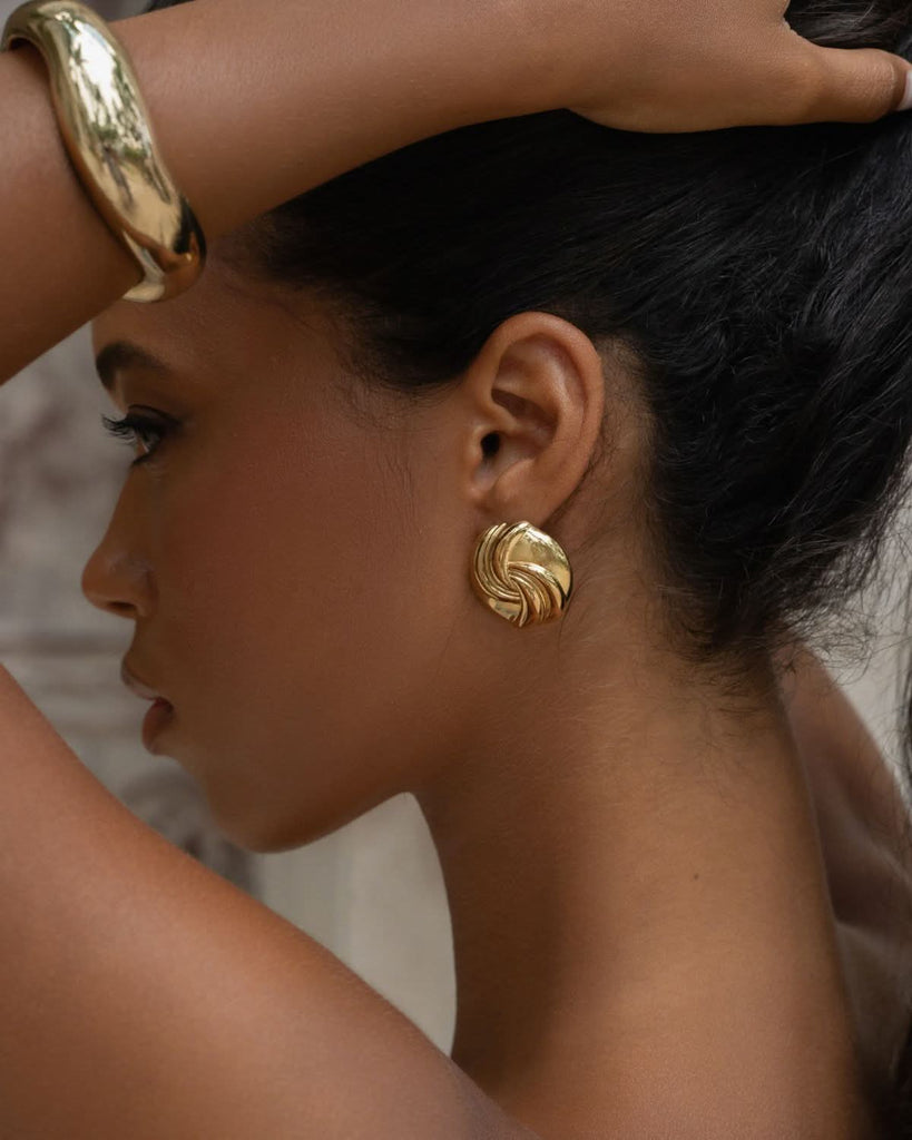 gold swirl earrings and bracelet on a dark skinned model