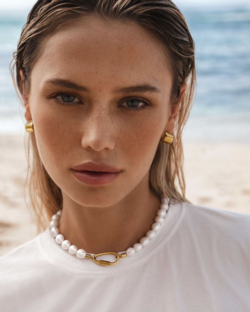 gold pearl carabiner necklace and gold earrings on a model