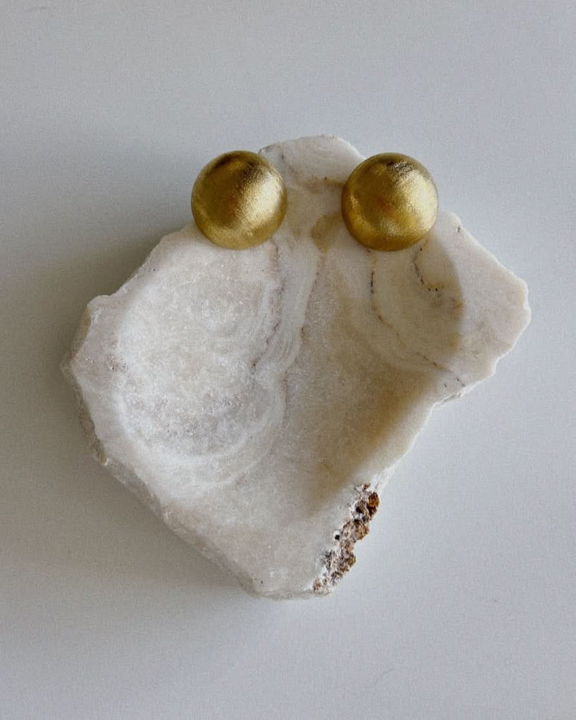 CULT OF SUN gold dome earrings on a stone tray