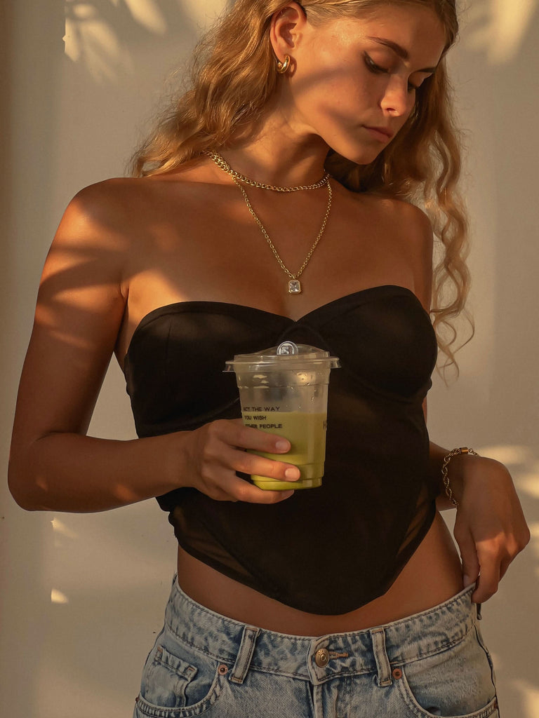 a girl wearing gold corset and gold jewelry, drinking matcha 