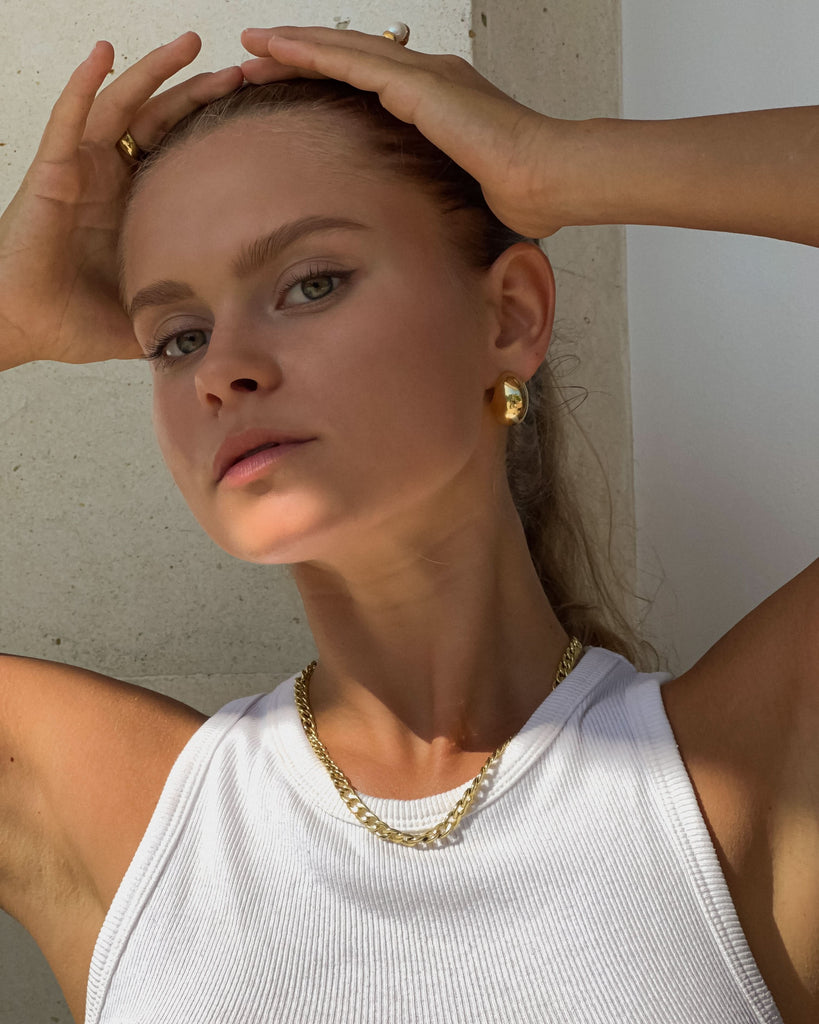 a glr in a tank top and gold earrings and necklace