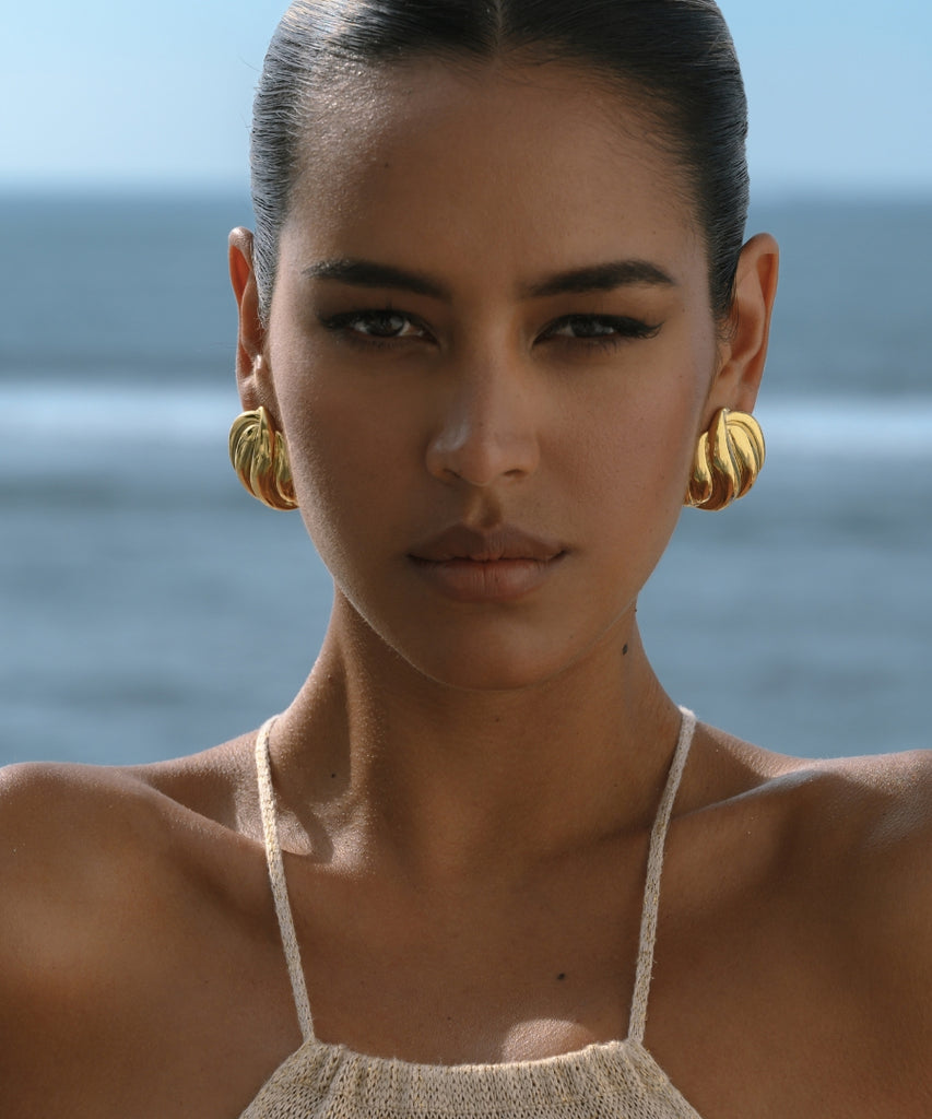 statement gold earrings on the model woth ocean at the background