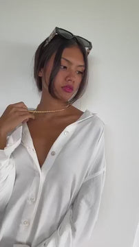 girl wearing long white button up and a single gold chain 