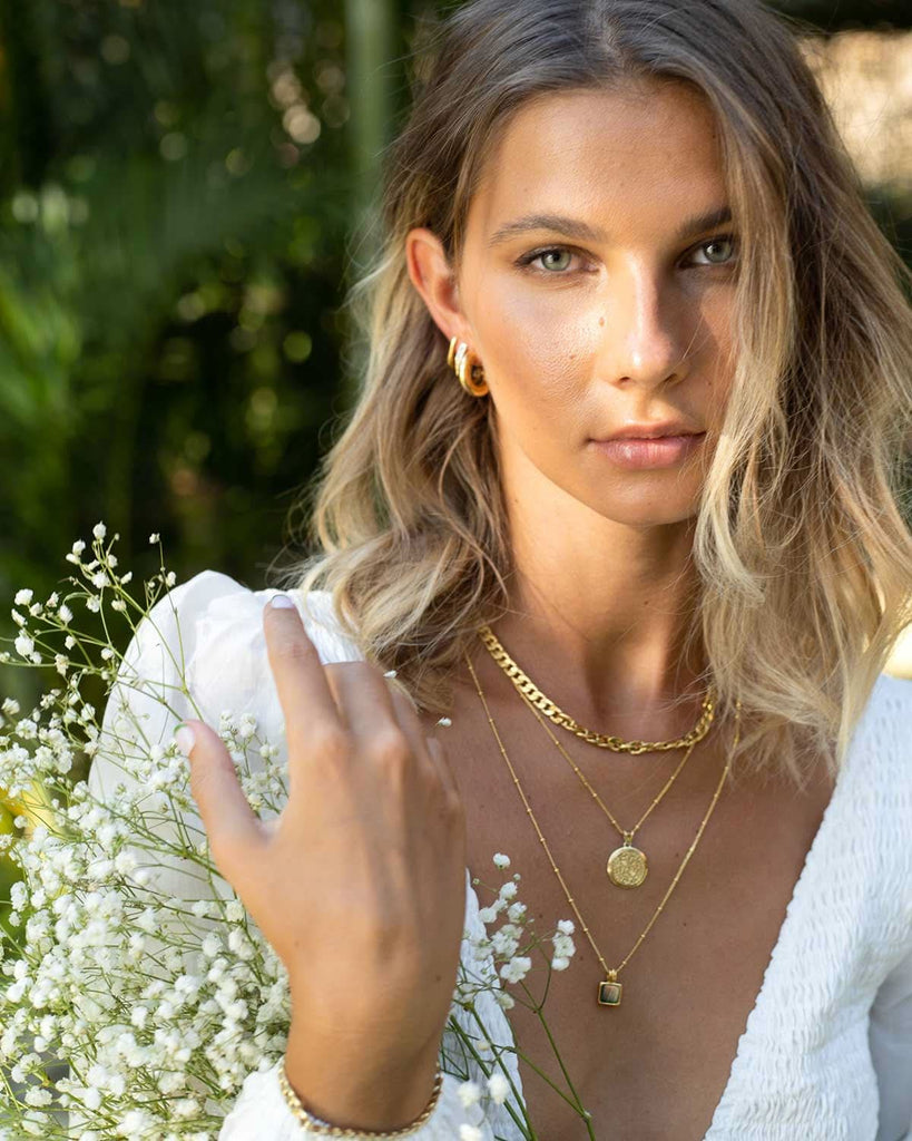 model in a garden wearing white with gold earrings and necklaces 