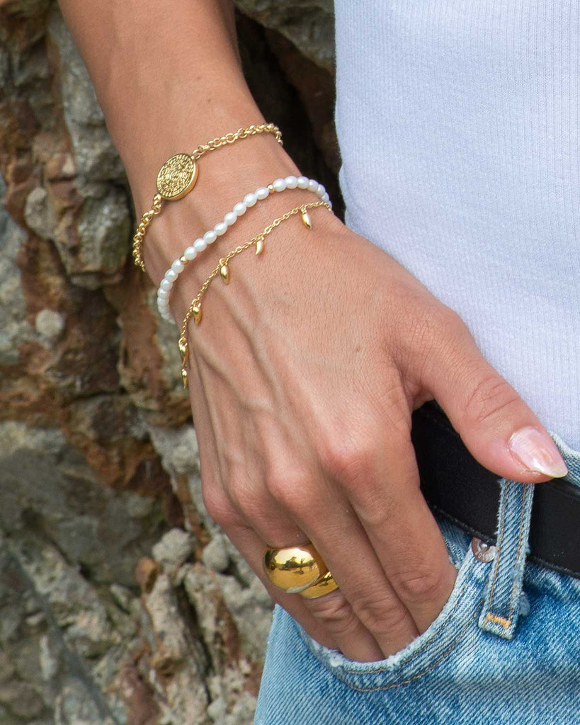 hand styled with a gold fang bracelet, pearl bracelet, aztec calendar bracelet, and gold dome rings 