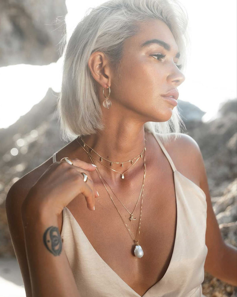 a large floating pear necklace layered with gold dainty necklaces