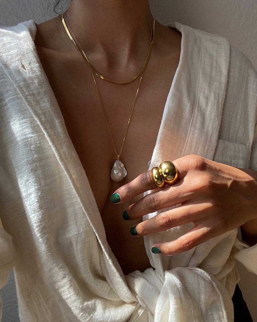 girl cleavage and hand wearing large pearl necklace and two gold rings stacked 