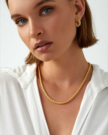 model wearing white blouse and single gold chain necklace