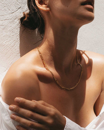 woman's neck, shoulder and cleavage from the side wearing a single gold chain