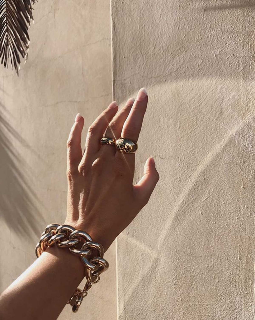 hand wearing chunky gold necklace and two dome rings 