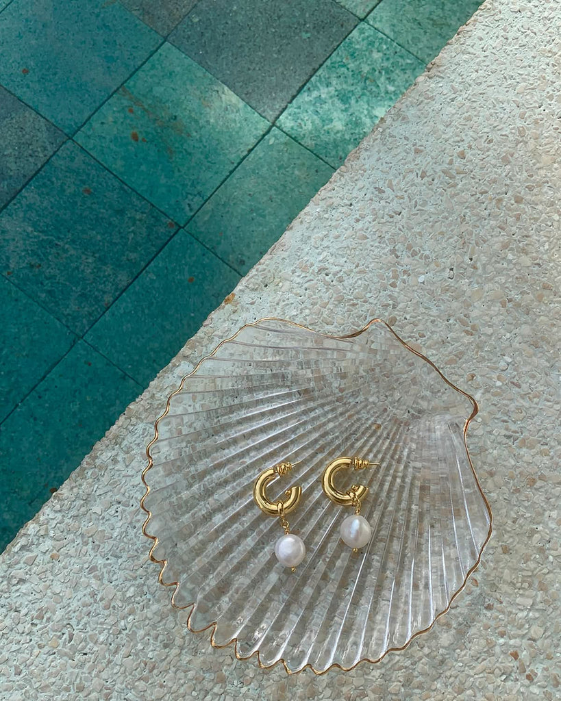 pearl earrings gold on a shell tray next to the pool