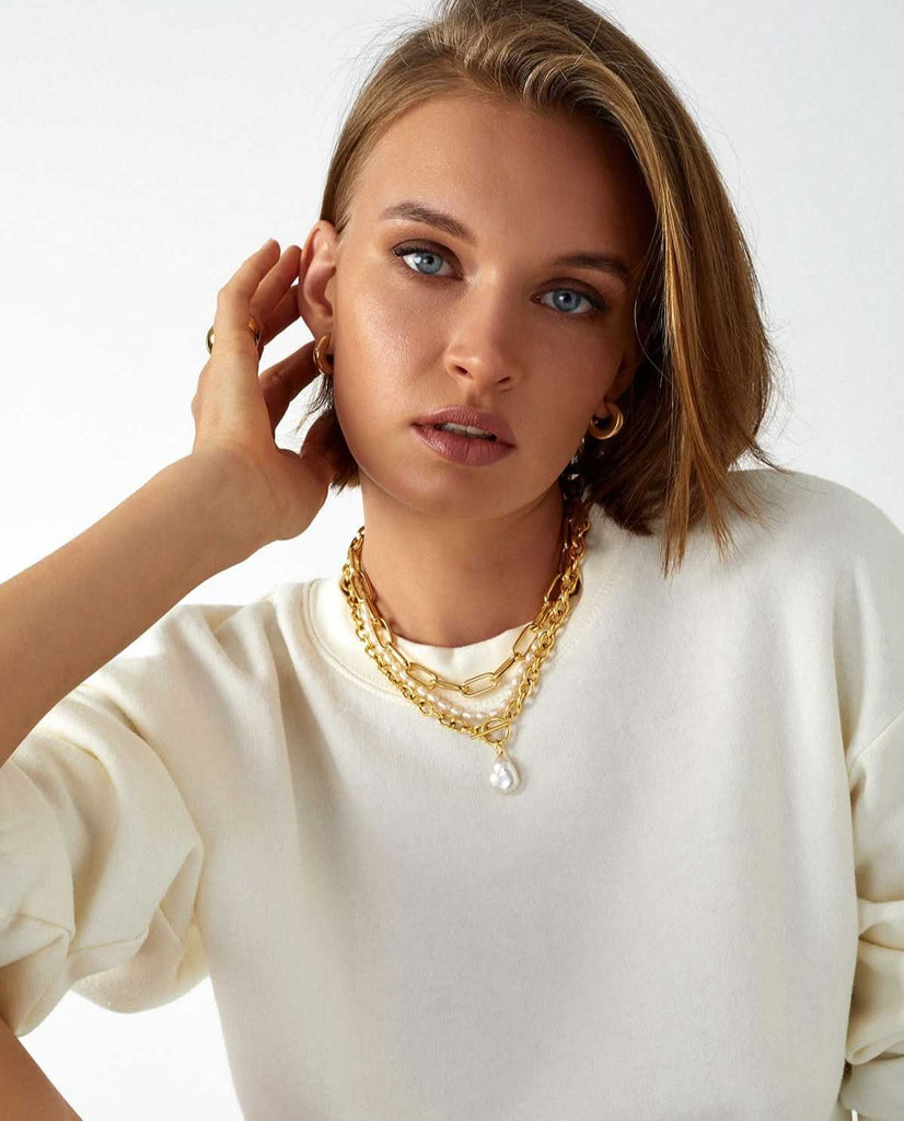 model wearing a white long sleeve and a mix of chunky chains & pearl layered necklaces