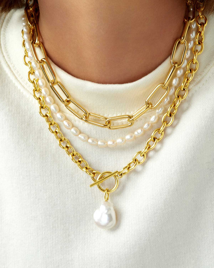 round neck white blouse featuring a chunky paperclip necklace, a large baroque pearl necklace, and a dainty pear necklace  