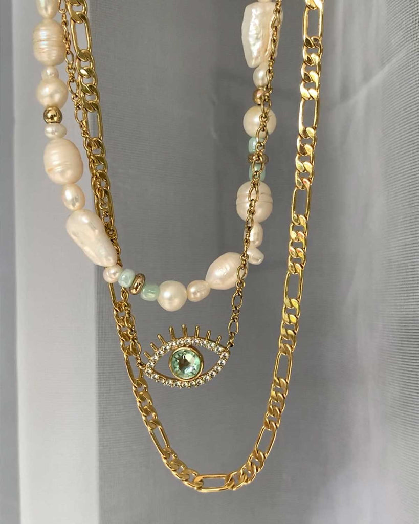 a pearl, an evil eye, and a golden necklace against white transparent fabric