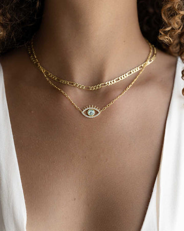 close up of girl's neck wearing a gold and a evil eye necklace