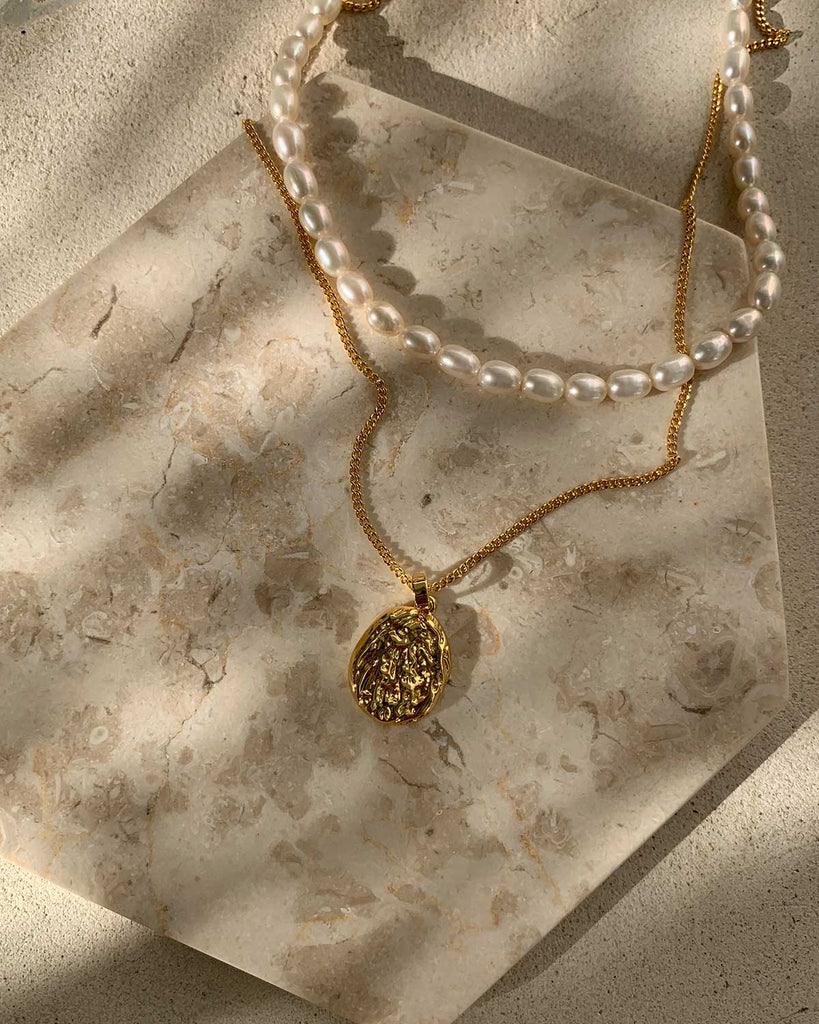 gold pendant and pearl necklace on marble