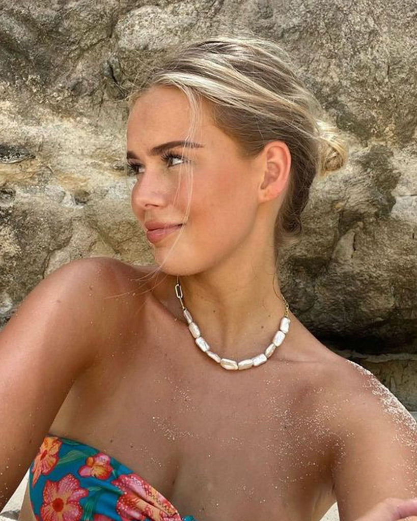 a girl wearing bikini and a pearl necklace sun bathing