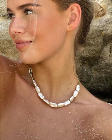 a girl wearing a pearl and gold chain necklace at the beach