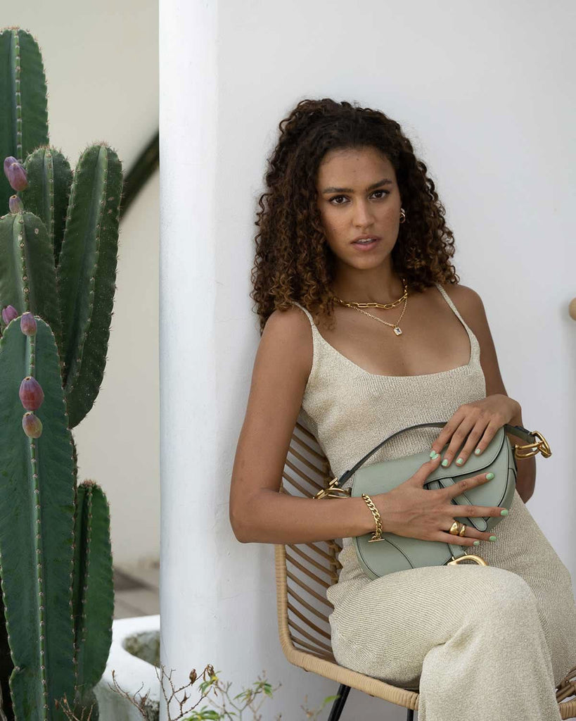 model seating down next to cactus featuring gold and light blue accessories 