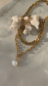 two chunky golden chains with one pearl placed on a coral 