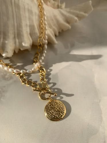gold aztect necklace and seed pearl necklace on a shell 